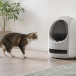 Adult cat approaching an unbranded automatic litter box beside a phone showing abstract trend lines